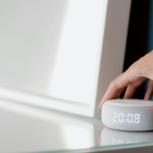 pexels-photo-4790257-4790257-1 Close-up of a hand adjusting a smart speaker displaying time indoors.